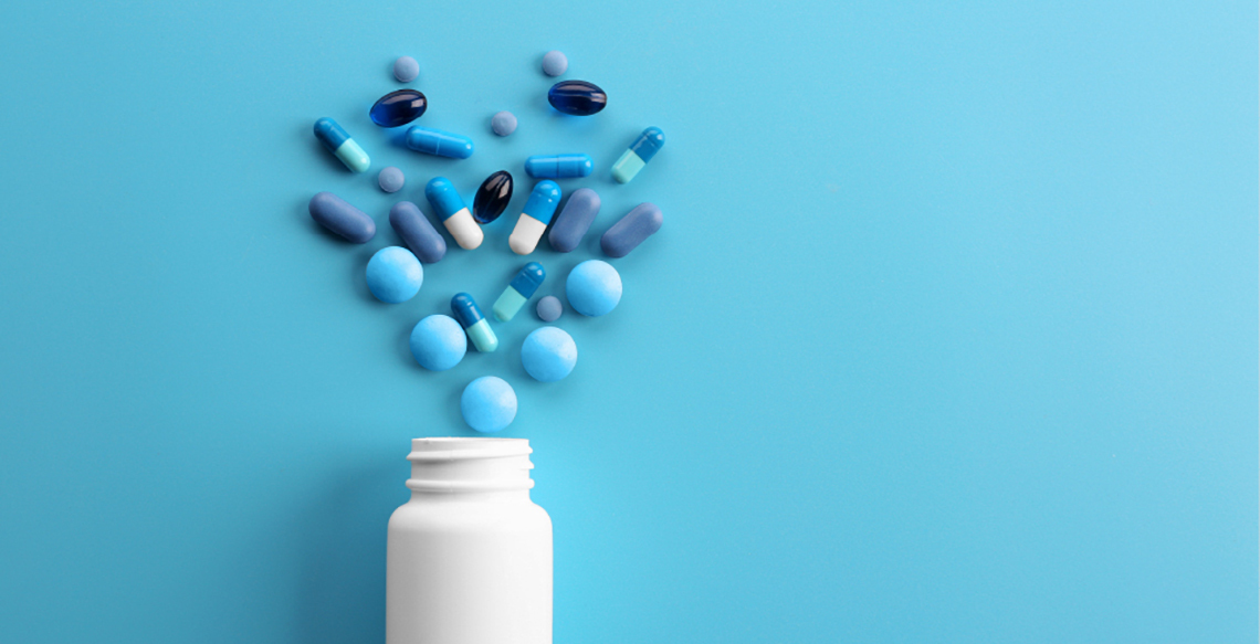 Blue background with White pill bottle and different shades of blue pills spilled out.