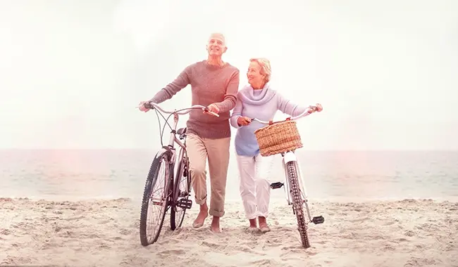 man and woman older couple walking bikes on the beach