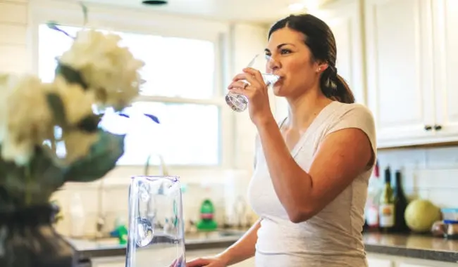 Woman drinking glass of water with flowers on the counter